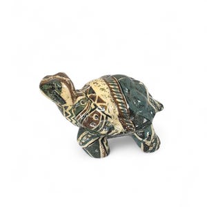 May include: A ceramic turtle figurine with a patterned shell in shades of green, brown, and cream. The turtle has a detailed design and is set against a white background. The figurine is a decorative item.