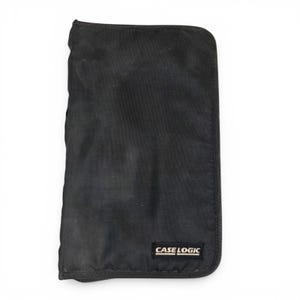 May include: Black Case Logic carrying case. The rectangular case is made of a durable, slightly textured fabric. The Case Logic logo is printed in white on a black rectangular label on the lower right corner of the case.