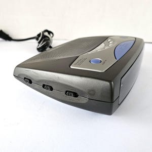 May include: A black and silver clock radio with a blue button and a small LCD screen. The radio has several buttons on the side, including "Sample", "Mute", and "Aux In".
