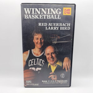 May include: A VHS video cassette with a black background featuring a photo of Red Auerbach and Larry Bird. The text on the cassette reads "Winning Basketball" and "Kodak Video Programs".
