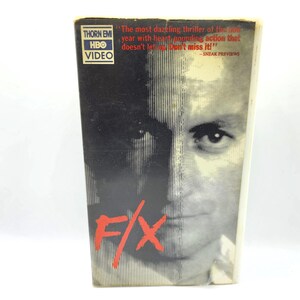 May include: A VHS tape case for the movie "F/X" with a black and white photo of a man's face on the front. The text "The most dazzling thriller of the year with heart-pounding action that doesn't let up. Don't miss it!" is printed on the case.
