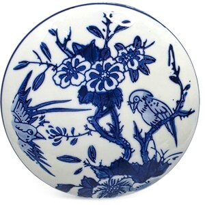 May include: A round, white ceramic plate with a blue floral and bird design. The plate features a central floral arrangement and two birds perched on branches. The design is a classic blue and white color scheme.