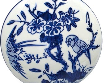 May include: A round, white ceramic plate with a blue floral and bird design. The plate features a central floral arrangement and two birds perched on branches. The design is a classic blue and white color scheme.