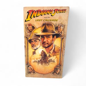 May include: Vintage VHS tape of "Indiana Jones and the Last Crusade." The cover features a portrait of Harrison Ford as Indiana Jones, along with other characters. The title is in yellow and red, set against a sepia-toned background.
