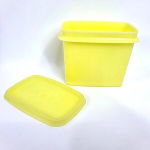 May include: A yellow plastic container with a matching lid. The container is rectangular with a slightly tapered shape. The lid is off to the side, revealing the inside of the container. The items are on a white background.