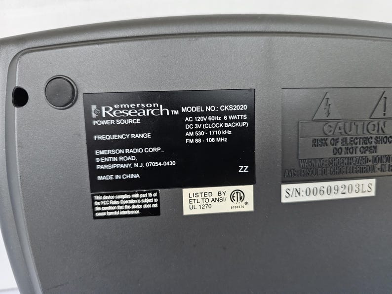 May include: A gray Emerson Research radio with a black label that reads "Research TM MODEL NO.: CKS2020", "POWER SOURCE", "FREQUENCY RANGE", "EMERSON RADIO CORP.", "9 ENTIN ROAD", "PARSIPPANY, N.J. 07054-0430", "MADE IN CHINA", "AC 120V 60Hz 6 WATTS", "DC 3V (CLOCK BACKUP)", "AM 530-1710 kHz", "FM 88-108 MHz", "LISTED BY ETL TO ANSI/ UL 1270", "ZZ", "CAUTION RISK OF ELECTRIC SHOCK DO NOT OPEN", "WARNING SHOCK HAZARD-DO NOT REMOVE COVER", "S/N:00609203LS".