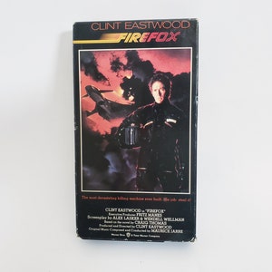 May include: A vintage VHS tape for the movie "Firefox" starring Clint Eastwood. The cover features a dramatic scene with a jet and a man in a black outfit against a red and black sky. Text includes the movie title and credits.