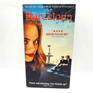 May include: A VHS video cassette cover for the movie "Barcelona" directed by Whit Stillman. The cover features a woman with long brown hair and a red lip, and two men in the background. The text on the cover reads "The sexy new comedy from the director of Metropolitan!" and "Barcelona".