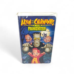 May include: A VHS tape titled "Alvin and the Chipmunks Meet Frankenstein." The cover features cartoon characters, including Alvin, Simon, Theodore, and Frankenstein's monster, set against a spooky night scene with a castle.