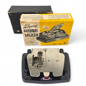 May include: A vintage Hollywood Automat Splicer, stainless steel, with its original box. The box is yellow and black with the product name and a picture of the splicer. The splicer is black and silver.