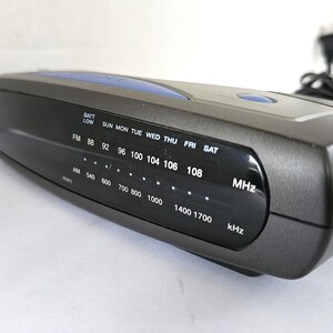 May include: A black and blue clock radio with a digital display showing the time, day of the week, and radio frequencies. The radio has a battery low indicator and a dial for tuning AM and FM frequencies.