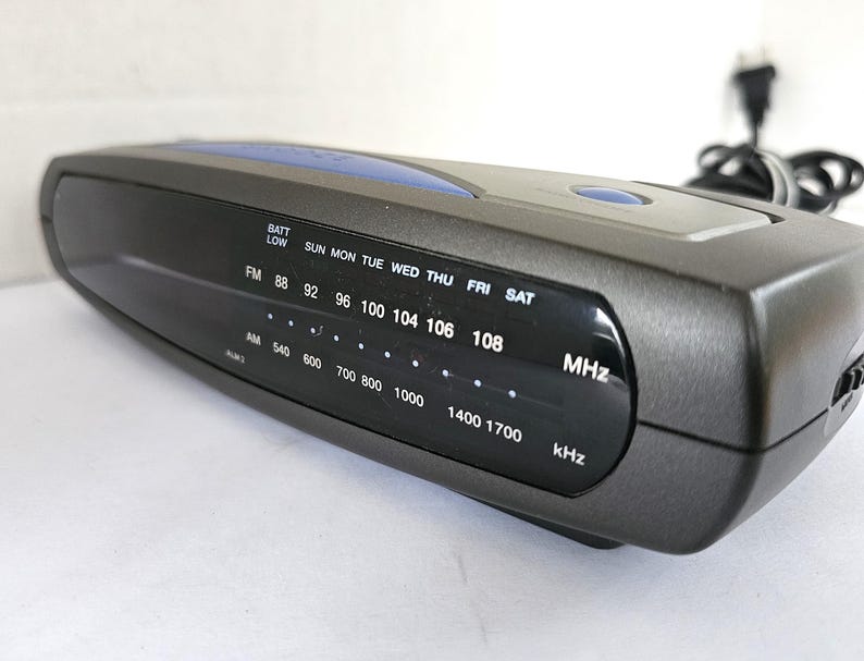 May include: A black and blue clock radio with a digital display showing the time, day of the week, and radio frequencies. The radio has a battery low indicator and a dial for tuning AM and FM frequencies.