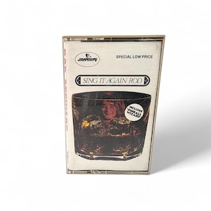 May include: A vintage cassette tape with the album cover of "Sing It Again Rod." The cover features a man inside a glass, with the text "Includes Pinball Wizard" and "Special Low Price."