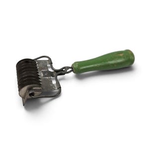 May include: A kitchen dough cutter featuring a series of circular metal blades attached to a wire frame and a cylindrical green wooden handle. The metal components show signs of wear and oxidation, while the handle has a smooth finish.