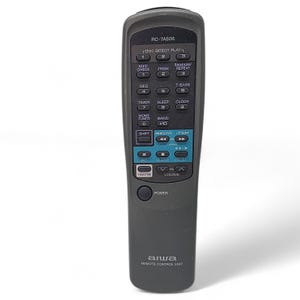 May include: A dark gray Aiwa remote control unit, model RC-7AS06, with numerous buttons for various functions. The buttons are labeled with text such as "Power," "Volume," and "Tuning." The remote is designed for audio equipment.