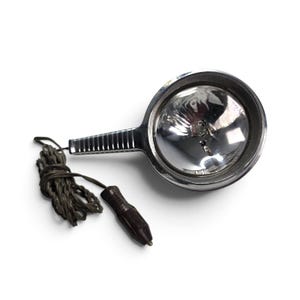 May include: A handheld chrome spotlight with a circular reflector and a ribbed handle. The lens features the text 12V. A dark brown coiled power cord is attached, ending in a standard automotive cigarette lighter plug for a 12-volt power source.