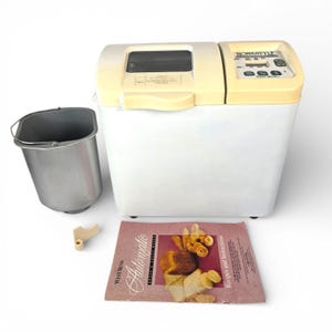 May include: A white and cream-colored West Bend Homestyle automatic bread maker with a digital display. Includes a metal bread pan, a beige paddle, and a recipe booklet. The bread machine is designed for home baking.
