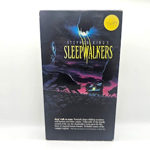 May include: A VHS tape cover for the horror movie "Sleepwalkers" by Stephen King. The cover features a dark background with a shadowy image of a cat and the title "Sleepwalkers" in yellow text.