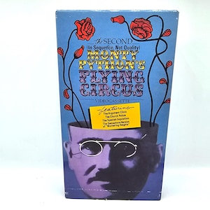 May include: A vintage VHS tape for "Monty Python's Flying Circus." The cover is blue with red roses and vines. The title is in gold and purple lettering. A yellow rectangle lists featured sketches. The image includes a stylized face with glasses.