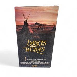 May include: A VHS tape of the movie "Dances With Wolves." The cover art features a landscape with teepees, a sunset, and the film's title in gold lettering. The tape also lists the film's Academy Award wins.
