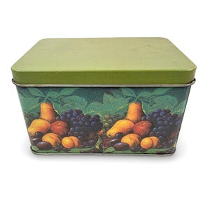 May include: A rectangular tin box with a green lid and a fruit design. The sides of the box feature illustrations of pears, grapes, peaches, and plums against a backdrop of green leaves. The box is likely used for storage.