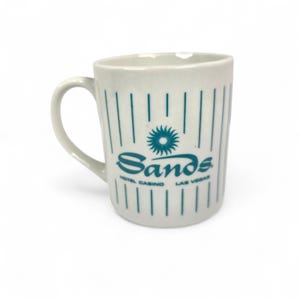 May include: White ceramic mug with teal vertical stripes and the word "Sands" in teal script. Below the word "Sands" is the text "HOTEL CASINO LAS VEGAS". A teal sunburst design is above the word "Sands".