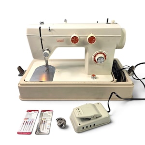 May include: A cream-colored Montgomery Ward sewing machine with orange control dials, a matching foot pedal, a metal bobbin case, and two packages of sewing machine needles. The machine features a metal needle plate and a sturdy base.