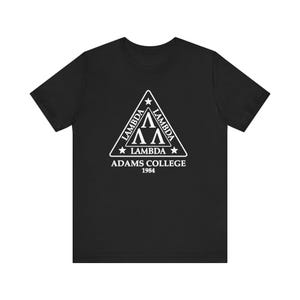May include: Black t-shirt featuring a white triangular design with the word "LAMBDA" on each side, and the Greek letters "ΛΛ" in the center. Below the triangle, the text reads "ADAMS COLLEGE 1984".