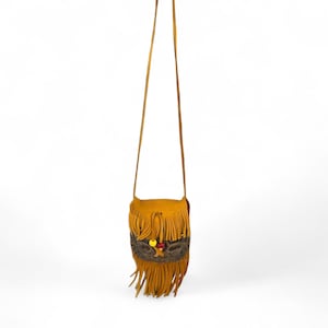 May include: A small, mustard-yellow crossbody bag with long, dangling fringe. The bag features a brown patterned band and is adorned with yellow and red beads. The strap is a thin, matching mustard-yellow color.