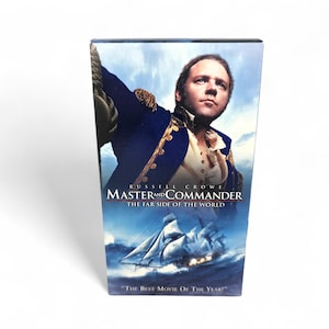 May include: A DVD case for the movie "Master and Commander: The Far Side of the World" featuring Russell Crowe. The cover art depicts a man in a naval uniform and a sailing ship on a stormy sea. The text "The Best Movie of the Year!" is at the bottom.