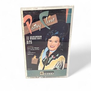 May include: A vintage Patsy Cline cassette tape. The cover features a portrait of Patsy Cline, with the text "Patsy Cline 12 Greatest Hits." The cassette case is clear plastic. The album includes songs like "Walkin' After Midnight" and "Crazy."
