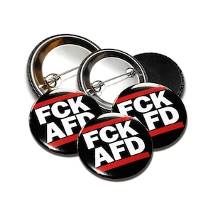 Könnte beinhalten: Vier schwarze und weiße Anstecknadeln mit einem roten Streifen. Die Nadeln zeigen "FCK AFD" in weißen Buchstaben.