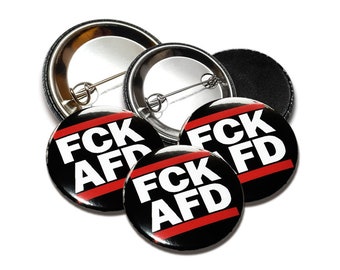 Könnte beinhalten: Vier schwarze und weiße Anstecknadeln mit einem roten Streifen. Die Nadeln zeigen "FCK AFD" in weißen Buchstaben.