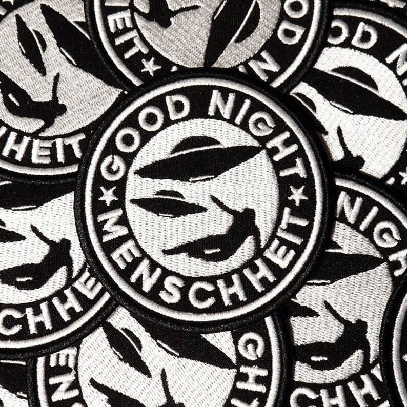Może przedstawiać: Naszywka haftowana w kolorze czarnym i białym z UFO i tekstem "Good Night Menschheit" w k&oacute;łku.