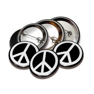 Könnte beinhalten: Vier schwarze und weiße Peace-Zeichen-Knöpfe mit silbernen Rückseiten. Die Knöpfe sind übereinander gestapelt.