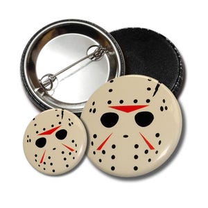 May include: Two button pins featuring a white hockey mask with black eyes and red accents. The larger pin is 2.25 inches in diameter and the smaller pin is 1.25 inches in diameter.