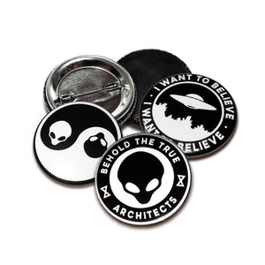 Könnte beinhalten: Vier schwarze und weiße Anstecknadeln mit verschiedenen Designs. Eine Nadel zeigt ein Yin-Yang-Symbol mit Alienköpfen, eine andere sagt "Ich will glauben" mit einem UFO, eine andere sagt "Betrachte die wahren Architekten" mit einem Alienkopf, und die letzte ist eine leere Nadel.