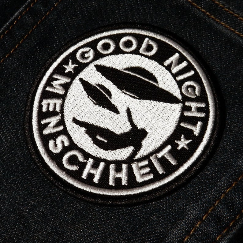 Może przedstawiać: Naszywka haftowana w kolorze czarnym i białym z tekstem "Good Night Menschheit" w k&oacute;łku.