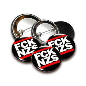 Op de afbeelding: Vier zwarte en rode knoopsluitingen met de tekst "FCK NZS" in witte letters. De knoopsluitingen zijn in een stapel gelegd met de achterkant van de knoopsluitingen naar boven.