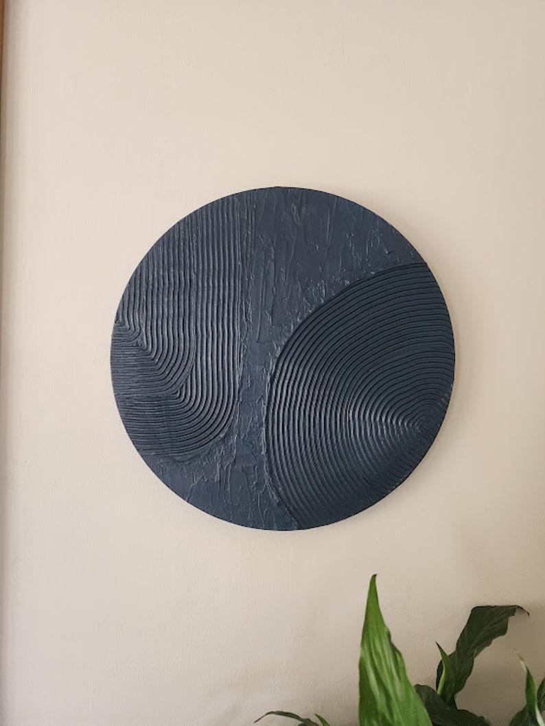 Puede incluir: Una decoraci&oacute;n de pared redonda de color azul oscuro con un dise&ntilde;o abstracto texturizado. El dise&ntilde;o presenta l&iacute;neas y curvas en relieve.