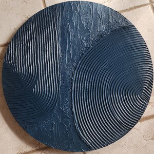 Puede incluir: Una decoraci&oacute;n de pared redonda de color azul oscuro con un dise&ntilde;o texturizado y abstracto. El dise&ntilde;o presenta una combinaci&oacute;n de l&iacute;neas curvas y patrones ondulados.