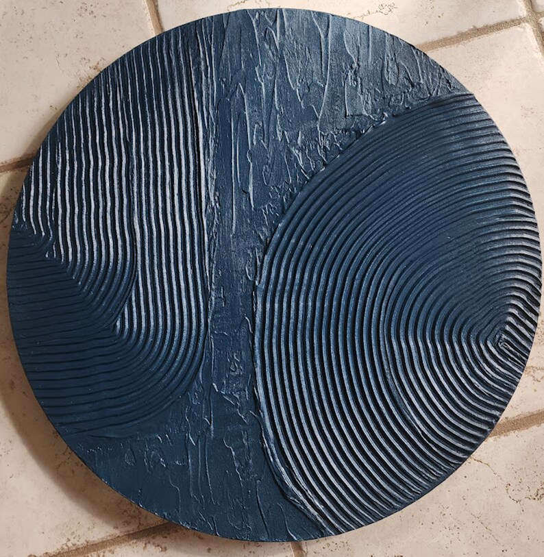 Puede incluir: Una decoraci&oacute;n de pared redonda de color azul oscuro con un dise&ntilde;o texturizado y abstracto. El dise&ntilde;o presenta una combinaci&oacute;n de l&iacute;neas curvas y patrones ondulados.