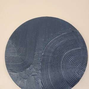 Puede incluir: Una decoraci&oacute;n de pared redonda de color azul oscuro con un dise&ntilde;o abstracto texturizado. El dise&ntilde;o presenta l&iacute;neas y c&iacute;rculos en relieve.