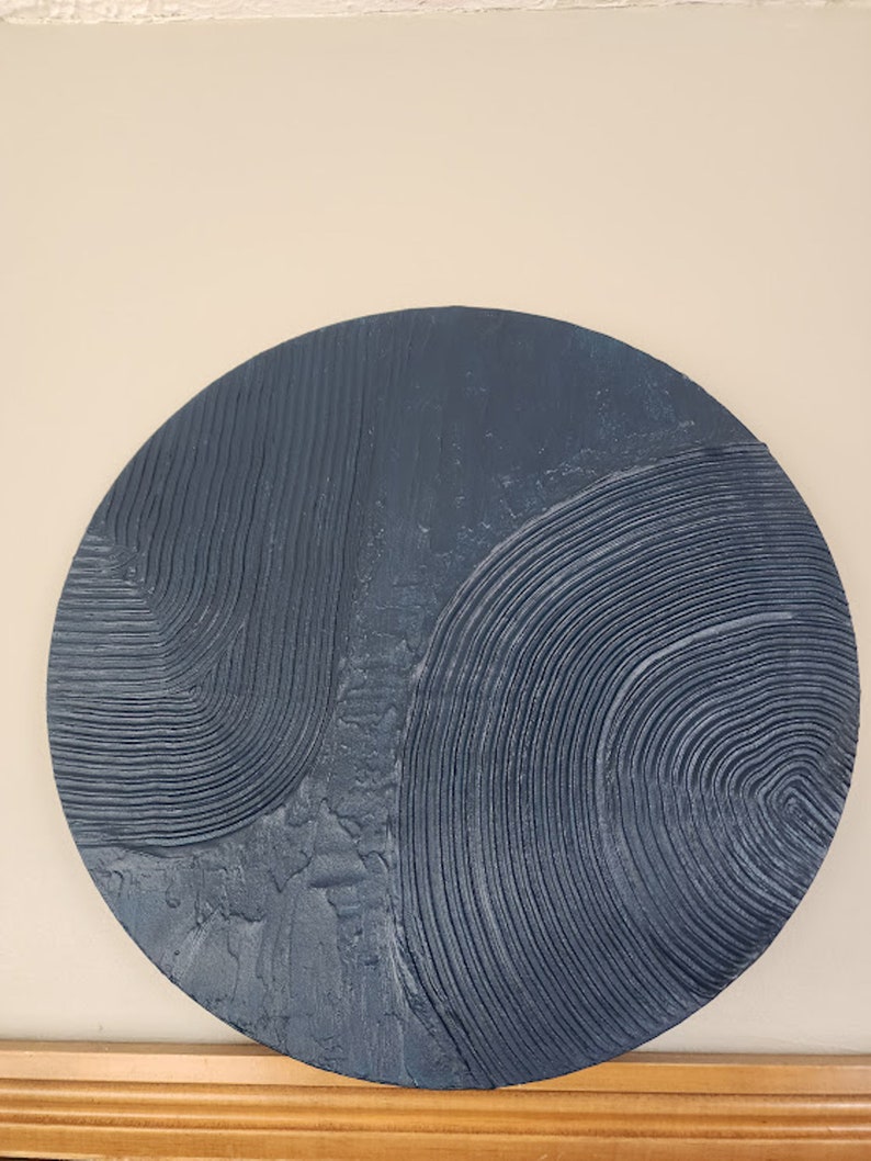 Puede incluir: Una decoraci&oacute;n de pared redonda de color azul oscuro con un dise&ntilde;o abstracto texturizado. El dise&ntilde;o presenta l&iacute;neas y c&iacute;rculos en relieve.