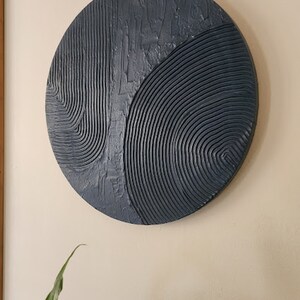 Puede incluir: Una escultura de pared circular con un dise&ntilde;o abstracto texturizado en tonos azules. La escultura est&aacute; hecha de un material que parece ser yeso o arcilla.
