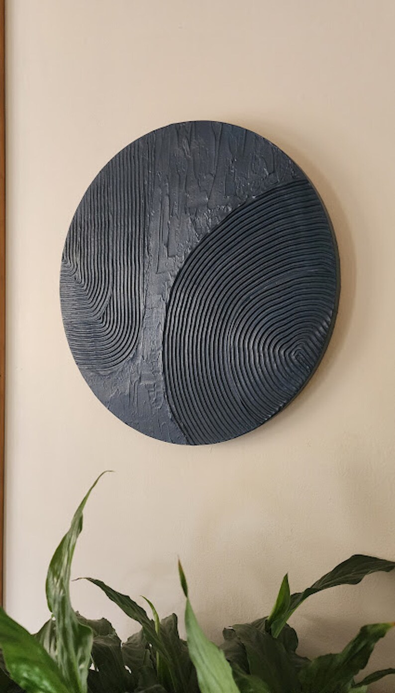 Puede incluir: Una escultura de pared circular con un dise&ntilde;o abstracto texturizado en tonos azules. La escultura est&aacute; hecha de un material que parece ser yeso o arcilla.