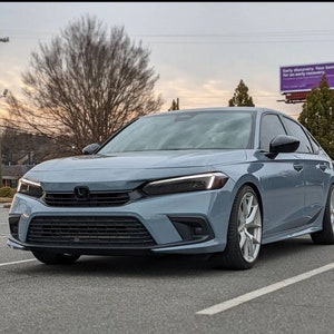 Może przedstawiać: Jasnoniebieski sedan Honda Civic z przyciemnionymi reflektorami i lampami tylnymi, czarnymi felgami i czarną kratką z logo Hondy.