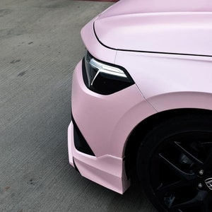 May include: A pink car with black wheels and a black front bumper. The car is parked in a car park.
