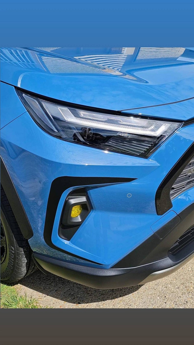K&ouml;nnte beinhalten: Ein blaues Auto mit schwarzen Zierleisten und einem gelben Blinklicht. Das Auto ist auf einer asphaltierten Fl&auml;che geparkt.