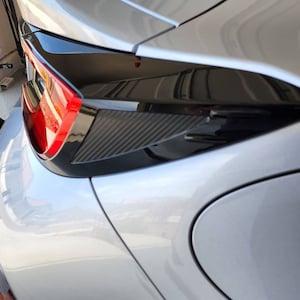 Puede incluir: Un coche plateado con un alerón trasero negro y una luz trasera roja. El coche está aparcado en un garaje.